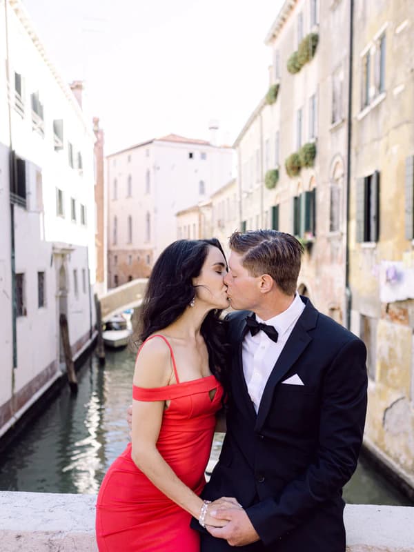 Couple kissing on a bridge over a narrow canal in Venice, with historic buildings lining the waterway