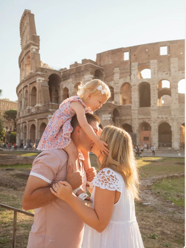 A couple lifts a young girl in front of the Colosseum in Rome